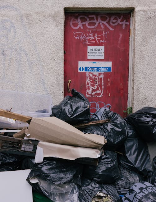 A pile of discarded waste materials and broken furniture located on a paved outdoor surface adjacent to a brick wall. The debris includes a wooden garden grate or trellis positioned upright, leaning a